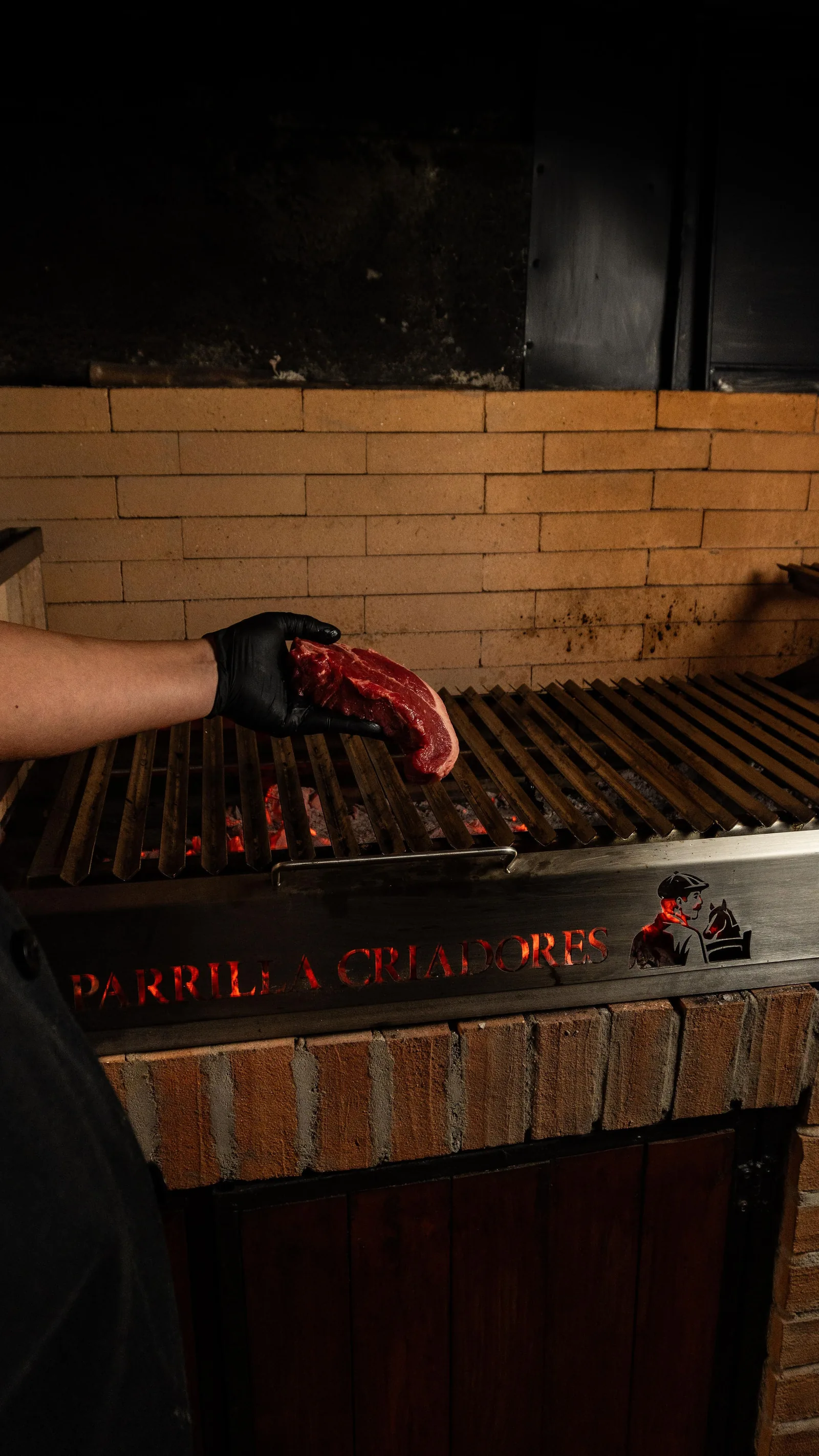 Parrillero sosteniendo un corte de carne sobre la parrilla de Parrilla Criadores